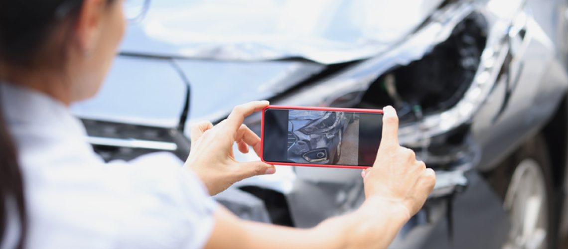 Insurance agent woman takes pictures by smartphone of car damage after road accident. Vehicle inspection and damage assessment concept