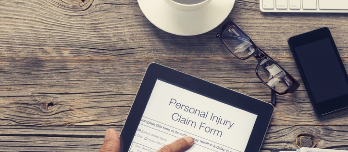 Personal injury claim form on a table. There is a keyboard, mobile phone and coffee on the old wooden table with pointing finger